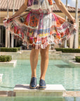 Woman standing on a stone ledge by a pool wearing 'Liz' Oxford shoes in Nuit Leather, paired with a colorful, airy dress, showcasing a blend of casual elegance.