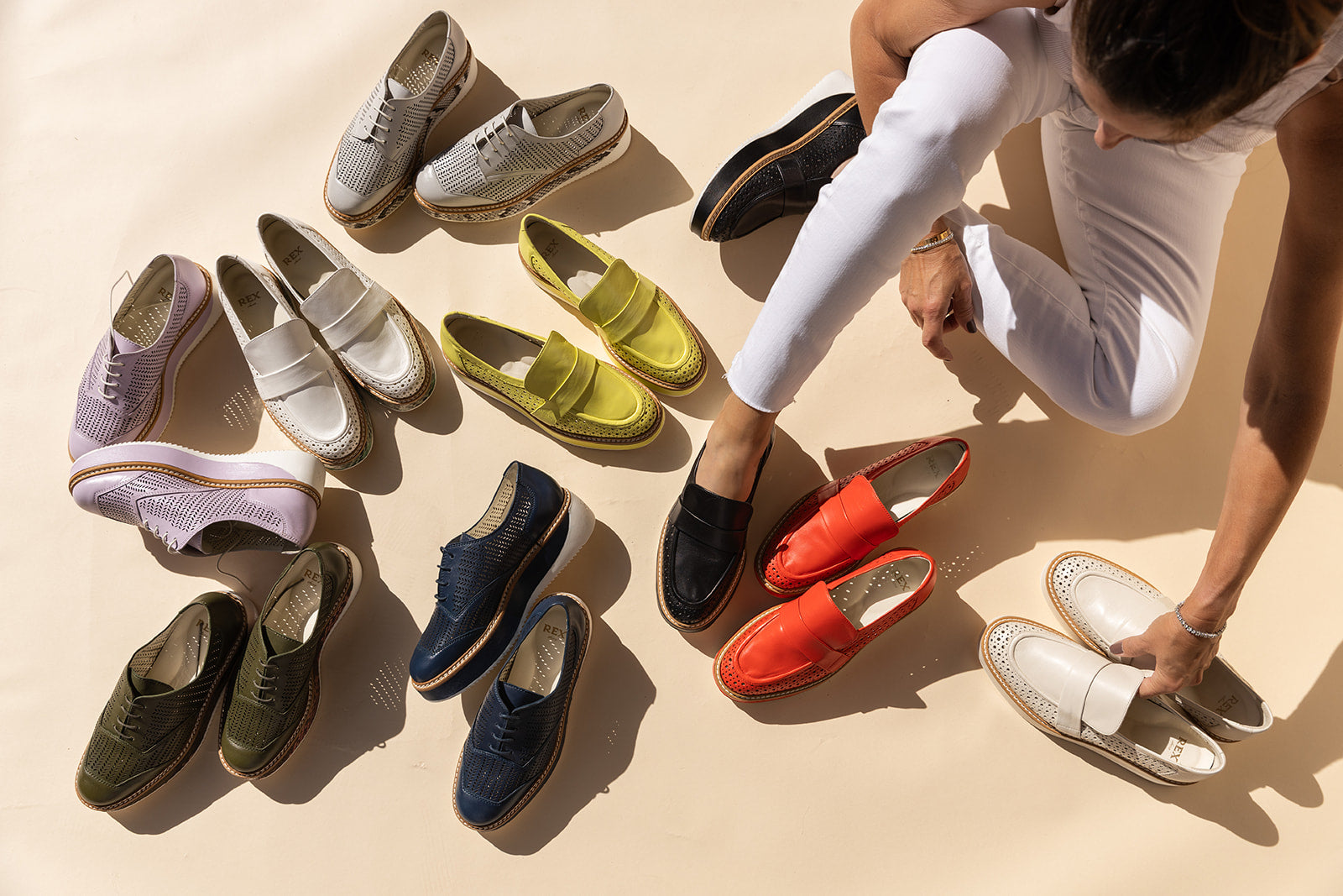 Assortment of Rex Shoes' luxury loafers for women in various colors, including classic white, vibrant red, and chic metallics, displayed around a stylish woman dressing up on a sunlit background.